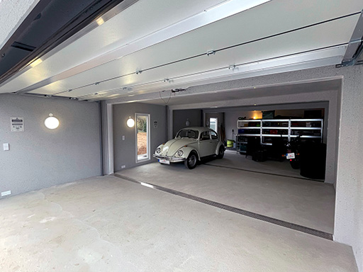 Eine großzügige, aufgeräumte Garage mit einem weißen klassischen Auto (VW Käfer) und modernen Regalsystemen im Hintergrund. Die Garage ist sauber und ordentlich gestaltet, mit gut beleuchteten Wänden und einer klaren Struktur.